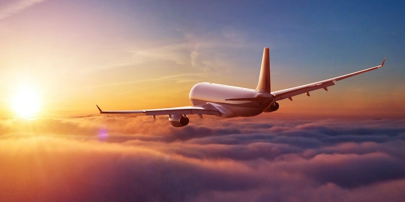 Un avión vuela sobre las nubes en dirección al sol que se acerca al horizonte.