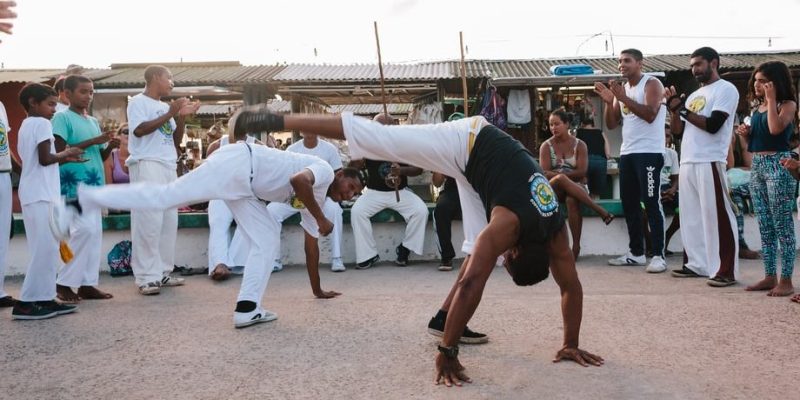 dos hombres practican capoeira rodeados de gente